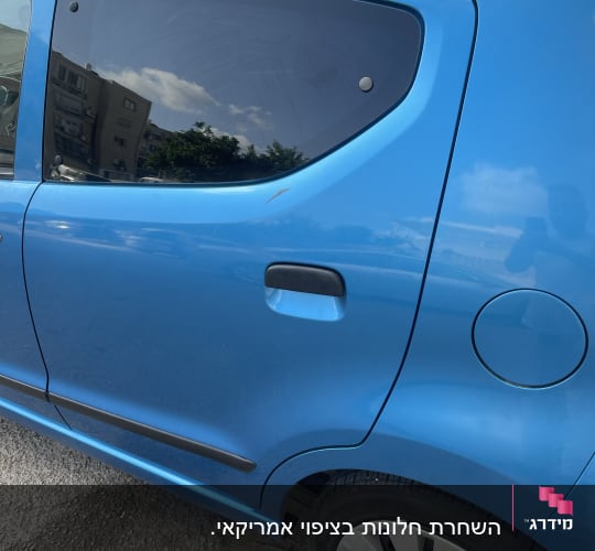 חלון אחורי כהה של רכב כחול עם השתקפות בניינים